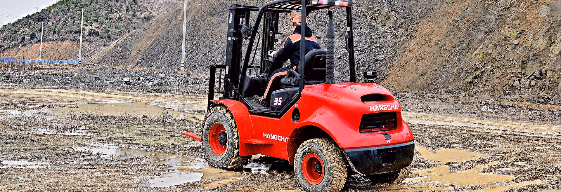 A person operates a red forklift on a muddy construction site.