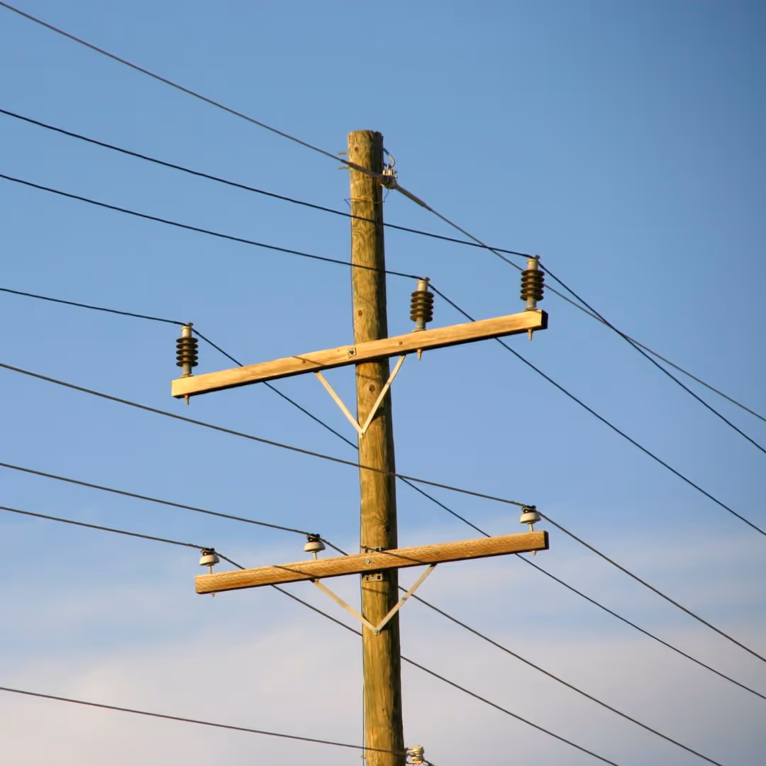 Wooden utility pole with multiple power lines against a clear blue sky.