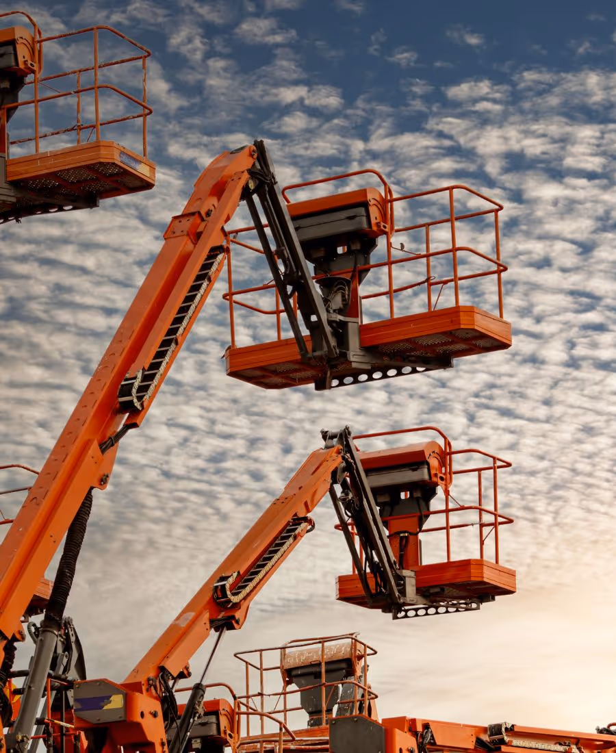 Orange construction lifts extend towards a cloudy sky